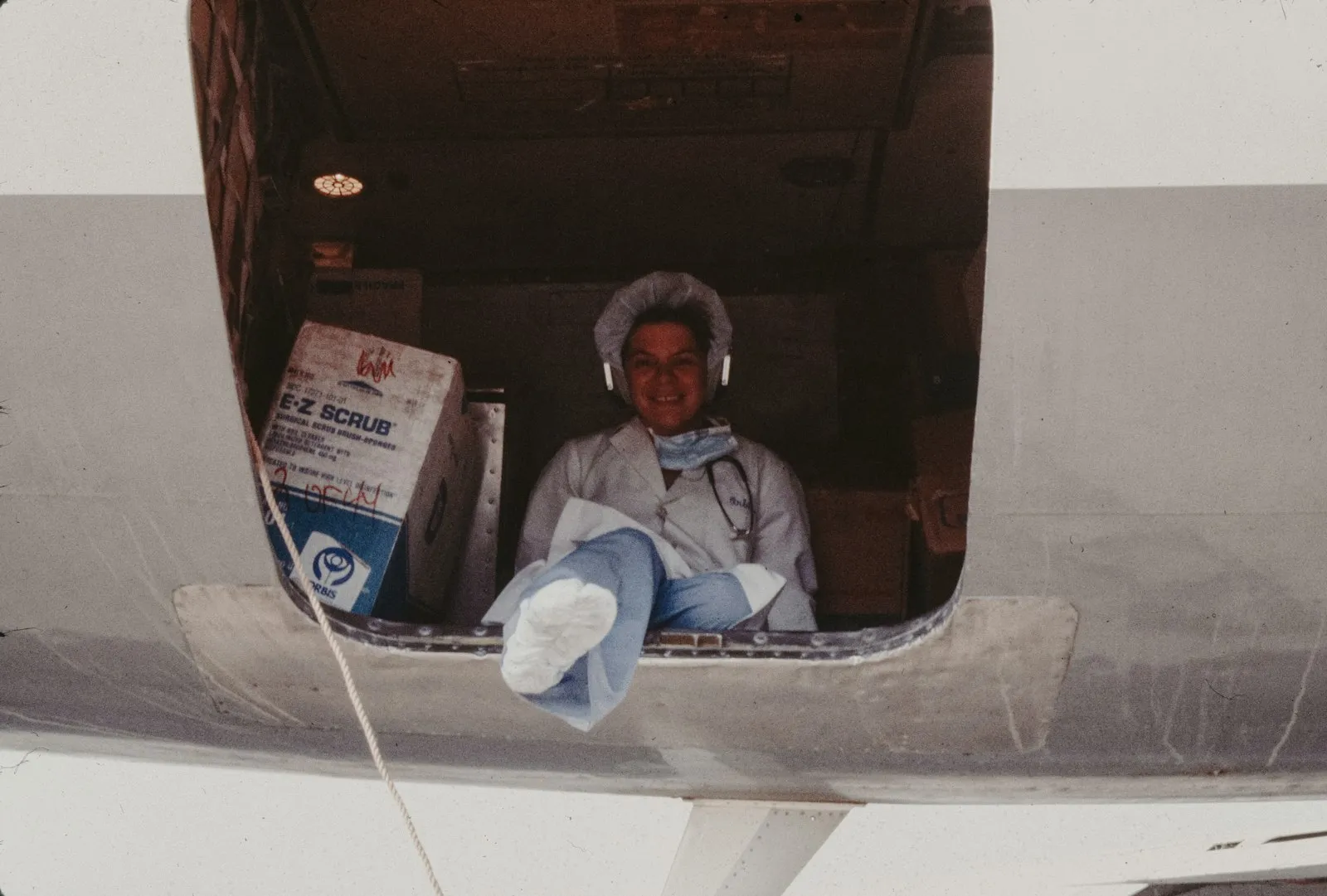 A doctor sitting in the hold of a cargo plane among boxes of medical supplies